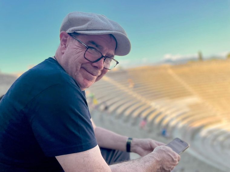 Michael Sutherland, seated in the stone tiers of an ancient amphitheatre, looking towards the camera